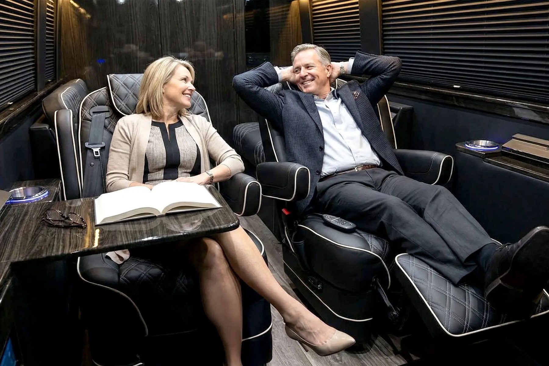 Two executives seated in reclining quilted leather captain's chairs inside the MA1 luxury Sprinter coach