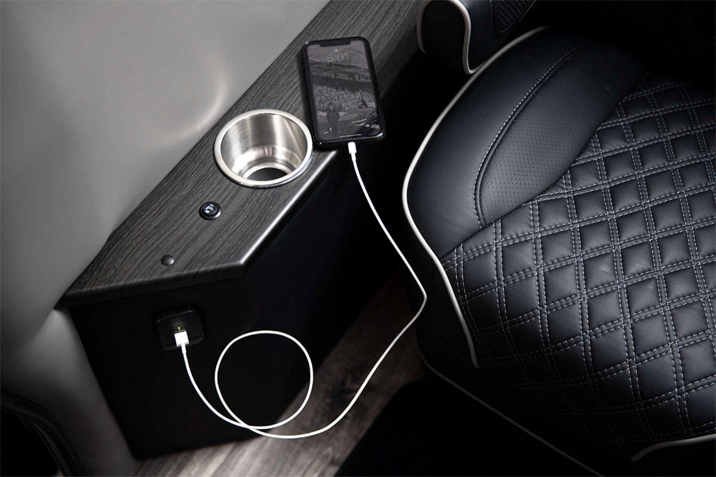 Seat-side console with cup holder and a phone charging from an outlet